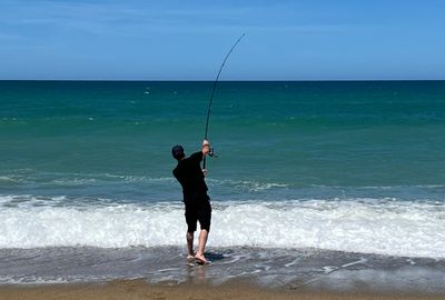 A man casts his line into the surf.